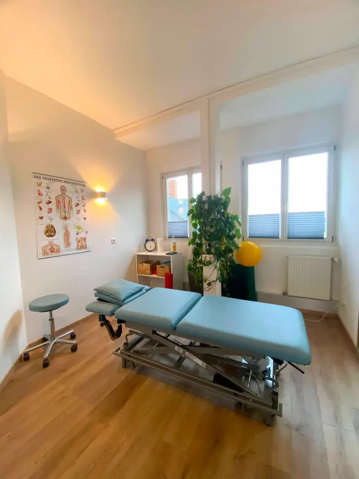 Heller Behandlungsraum mit türkiser Therapieliege